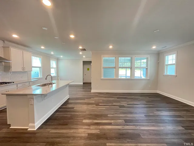 a large white kitchen with kitchen island a sink wooden floor and a living room