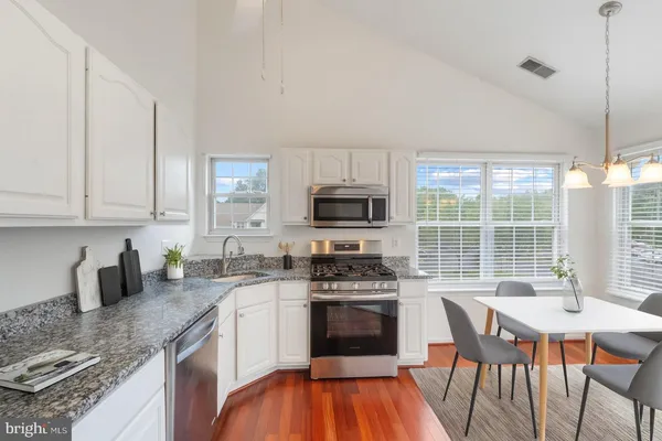 a kitchen with stainless steel appliances granite countertop a stove a sink a microwave a refrigerator and white cabinets with wooden floors