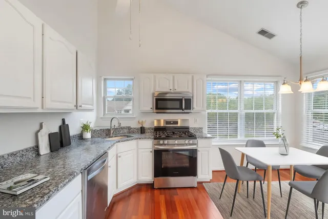 a kitchen with stainless steel appliances granite countertop a stove a sink a microwave a refrigerator and white cabinets with wooden floors