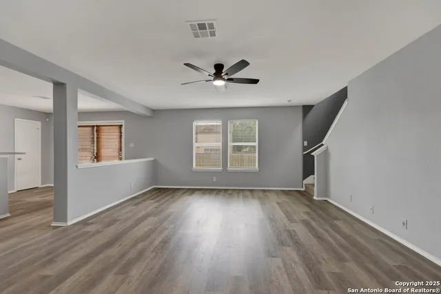 an empty room with wooden floor chandelier fan and windows