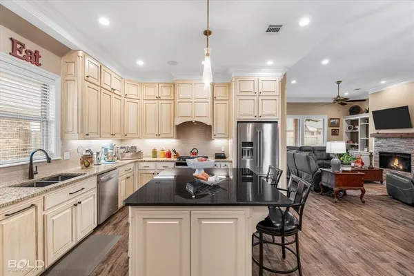 a kitchen with stainless steel appliances granite countertop a refrigerator a sink dishwasher a dining table and chairs with wooden floor