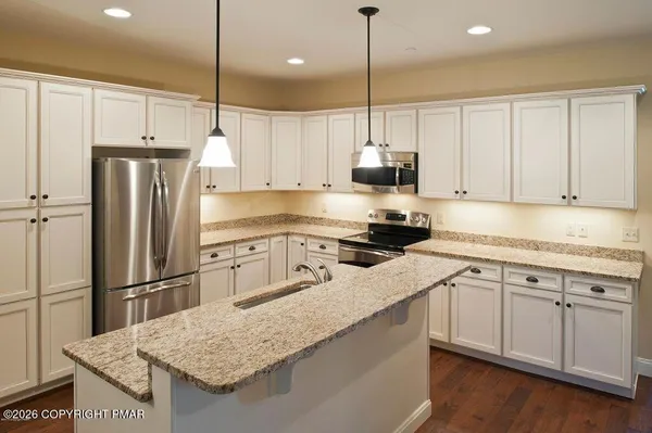 a kitchen with stainless steel appliances granite countertop a refrigerator a sink dishwasher a stove and white cabinets with wooden floor