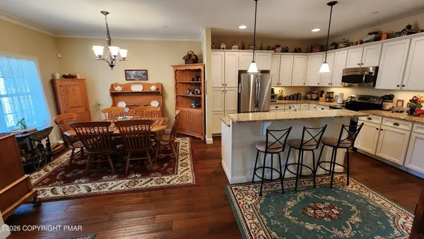 a kitchen with stainless steel appliances granite countertop a stove a refrigerator a kitchen island a dining table and chairs with wooden floor