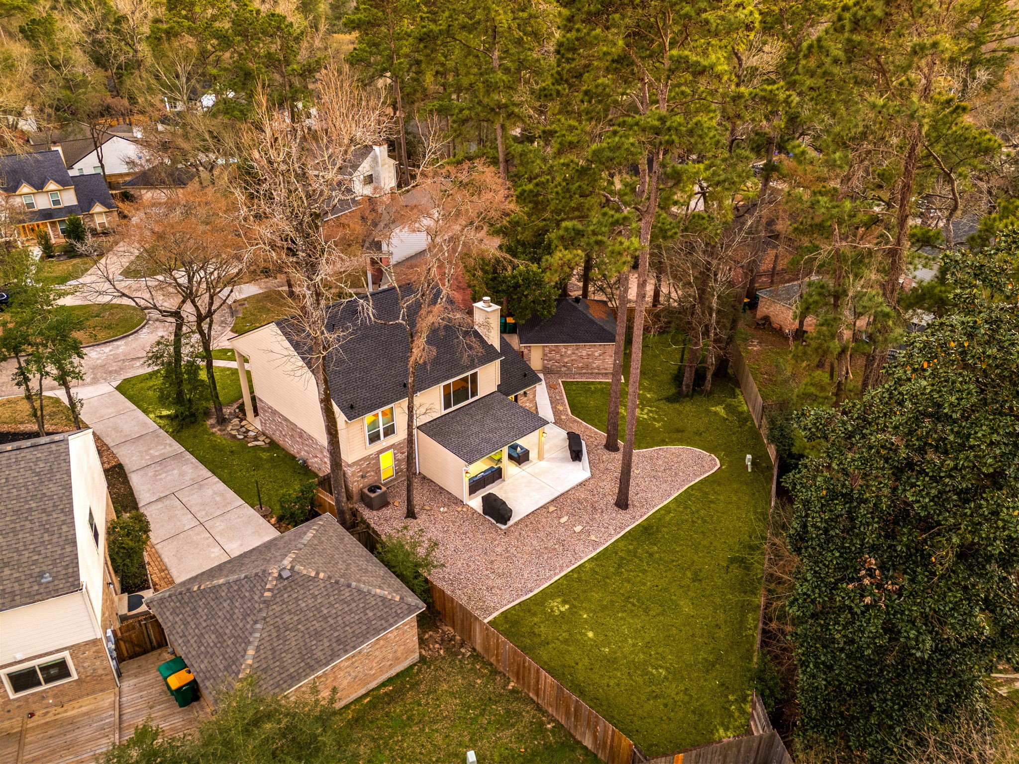 57 Fire Flicker Place Spring, TX 77381 - Photo 4 of 11 This aerial view showcases a charming 4-bedroom home surrounded by tall trees, featuring a spacious backyard with a covered, paved patio area. The property is situated on a quiet street with neighboring houses, offering a serene and private setting ideal for family living.