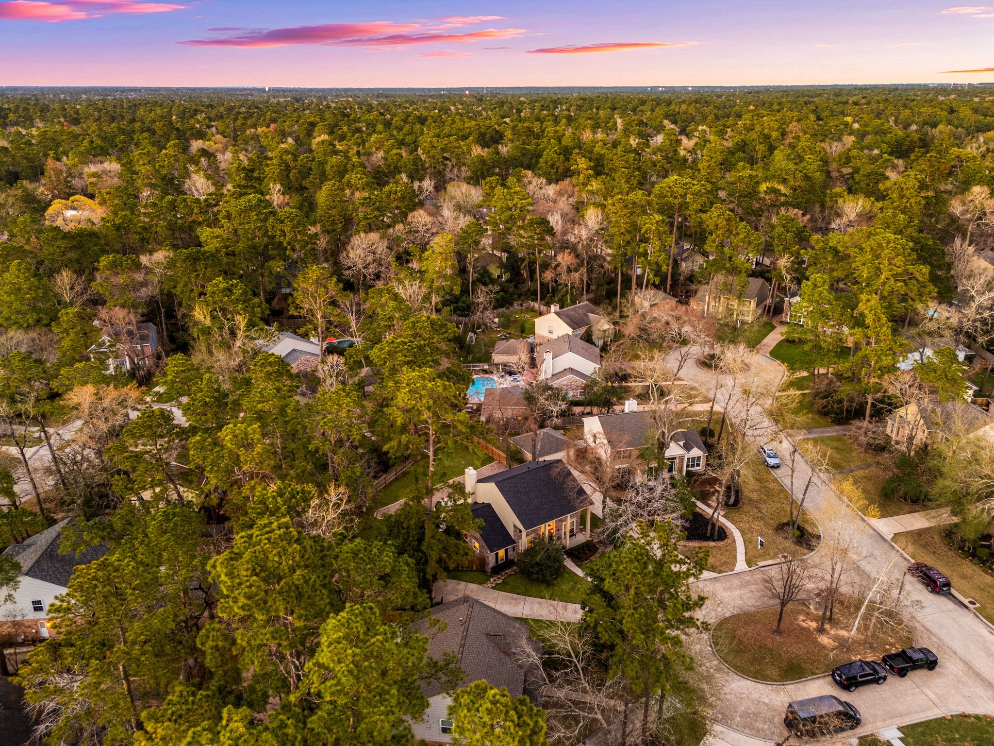 57 Fire Flicker Place Spring, TX 77381 - Photo 10 of 11 This aerial view showcases a peaceful residential neighborhood surrounded by lush trees, offering a serene and private setting. The homes are well-spaced with a mix of architectural styles and check out that gorgeous black roof on 57 Fire Flicker! The sunset in the background adds a warm and inviting ambiance. The front door faces South.