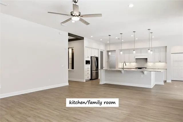a view of kitchen with stainless steel appliances granite countertop a refrigerator a sink a stove and white cabinets with wooden floor