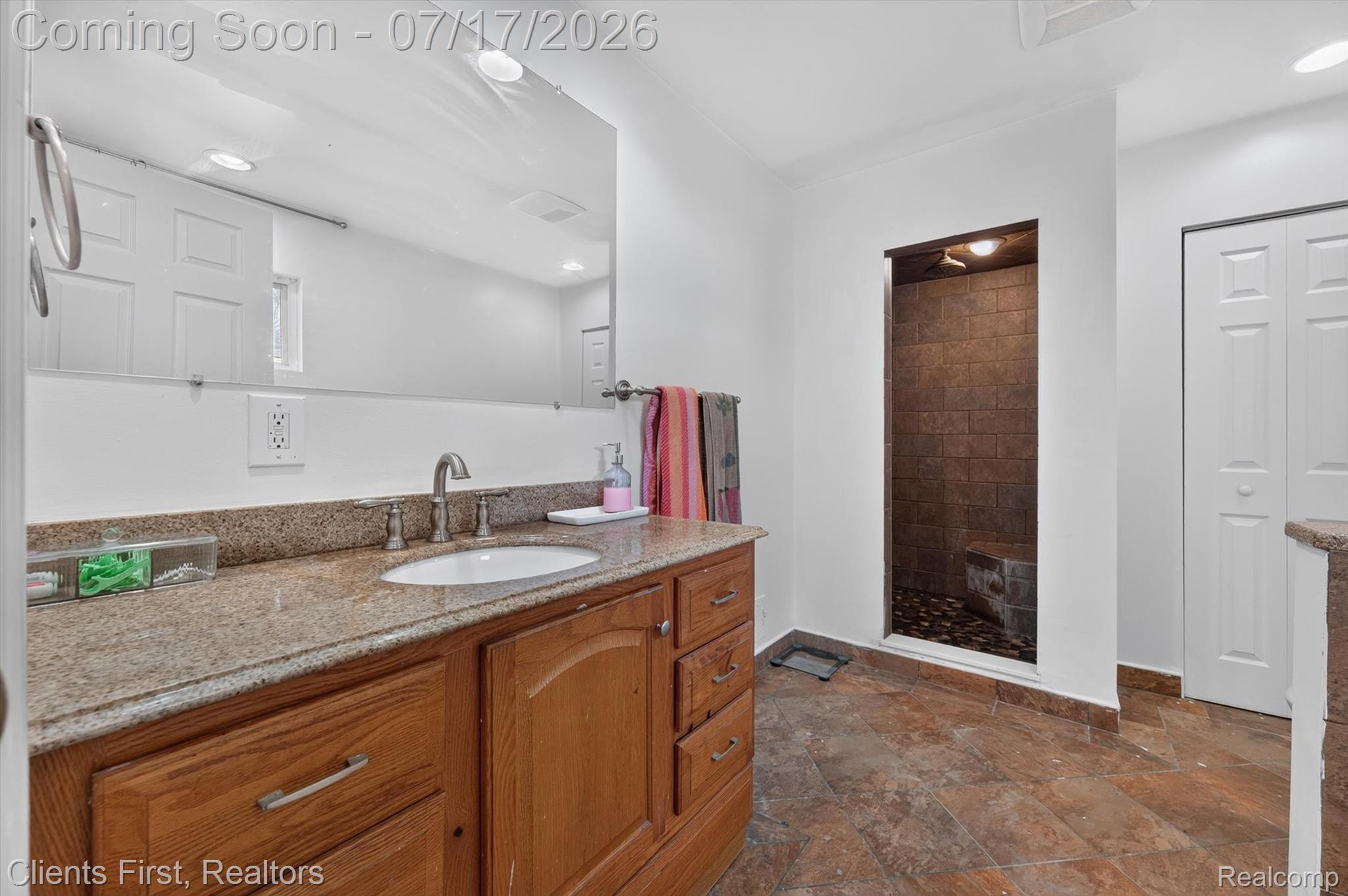 36852 Chase Street Romulus, MI 48174 - Photo 26 of 40 Bathroom featuring a granite-topped vanity with a single basin, a walk-in shower with stone tile walls and a pebble floor, and white paneled bifold doors