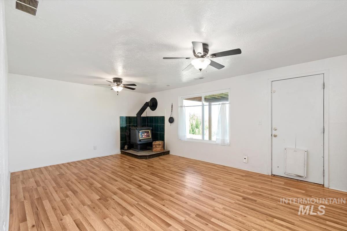 10178 West Fox Ridge Drive Boise, ID 83709 - Photo 18 of 36 Spacious room featuring wood-finish flooring, a corner wood-burning stove with a tiled surround, and multiple ceiling fans