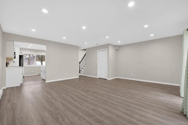 a view of an empty room with wooden floor and a kitchen