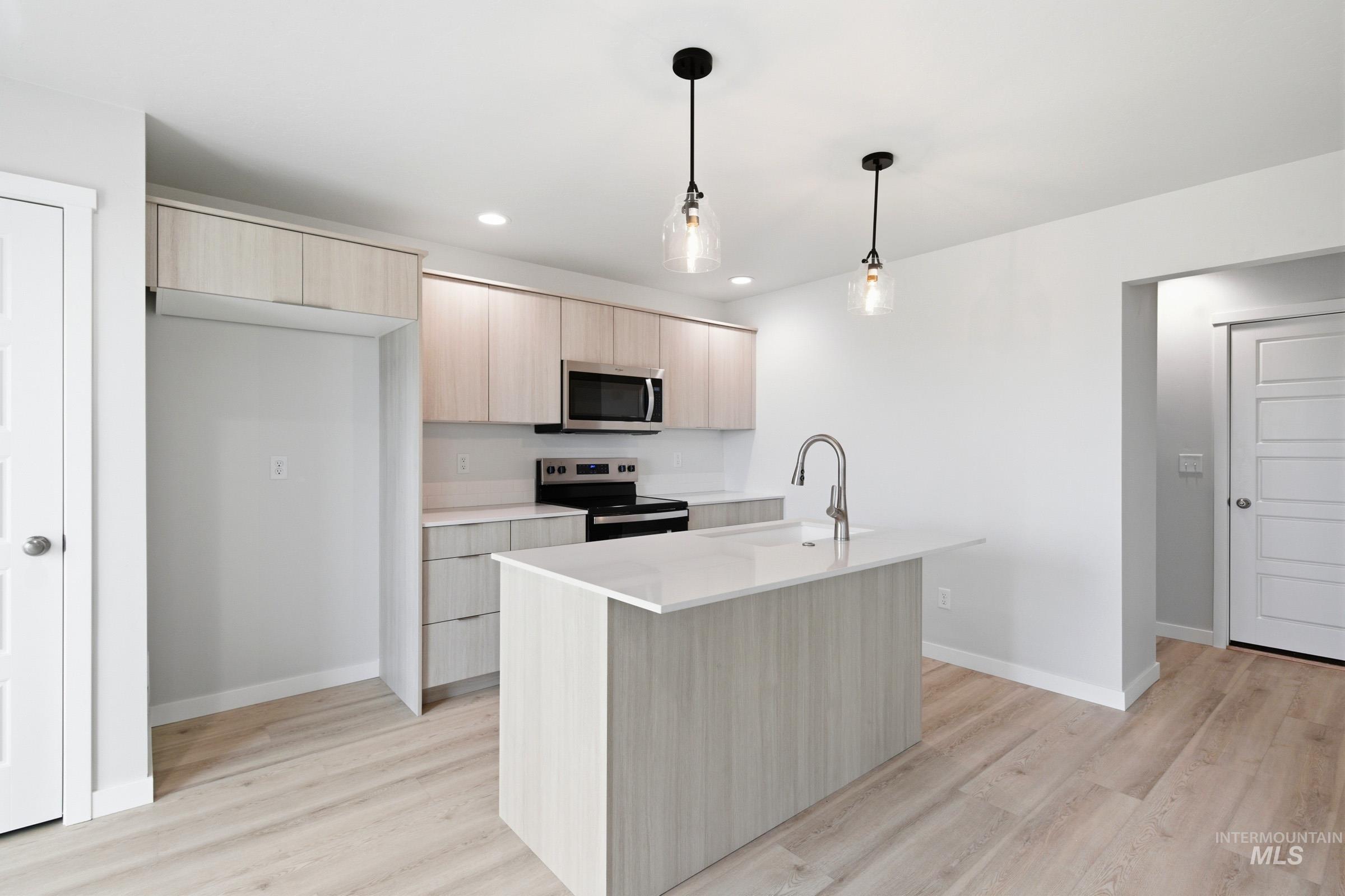 10788 Rutland Street Caldwell, ID 83605 - Photo 3 of 22 Kitchen featuring light wood finish cabinets, hanging light fixtures, stainless steel appliances, light wood finished floors, and a center island with sink