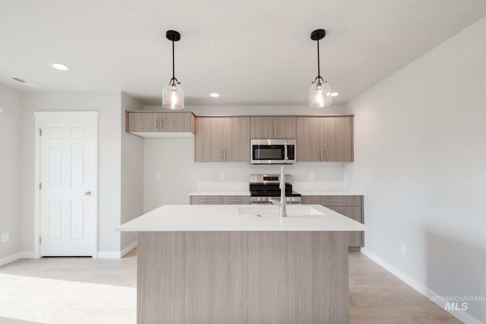 10788 Rutland Street Caldwell, ID 83605 - Photo 4 of 22 Kitchen with modern cabinets, light wood finish cabinets, stainless steel appliances, hanging light fixtures, and light wood-style flooring