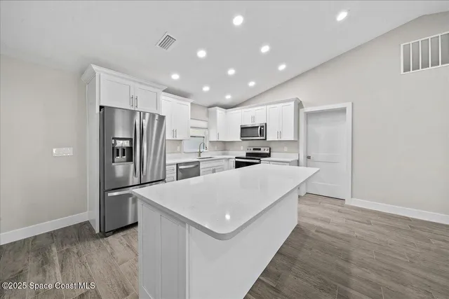 a large kitchen with kitchen island white cabinets stainless steel appliances a sink and wooden floor