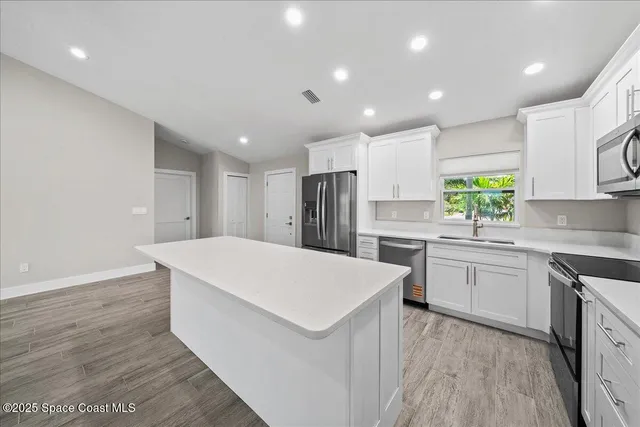 a kitchen with stainless steel appliances granite countertop grey cabinets a sink a stove a microwave and wooden floors