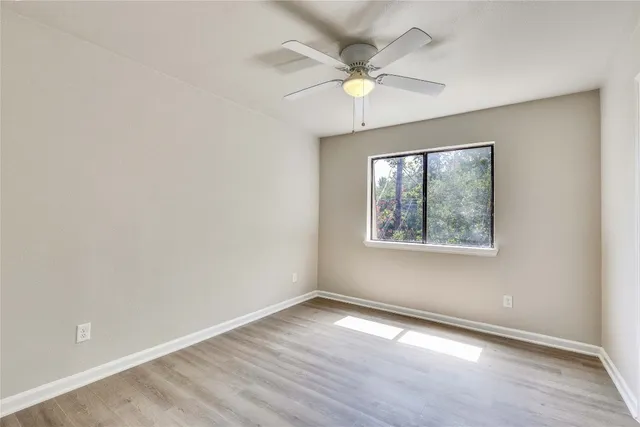 an empty room with wooden floor fan and windows