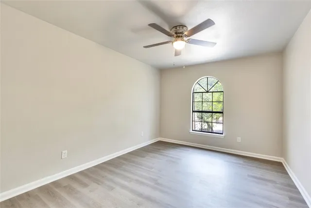 an empty room with wooden floor fan and windows