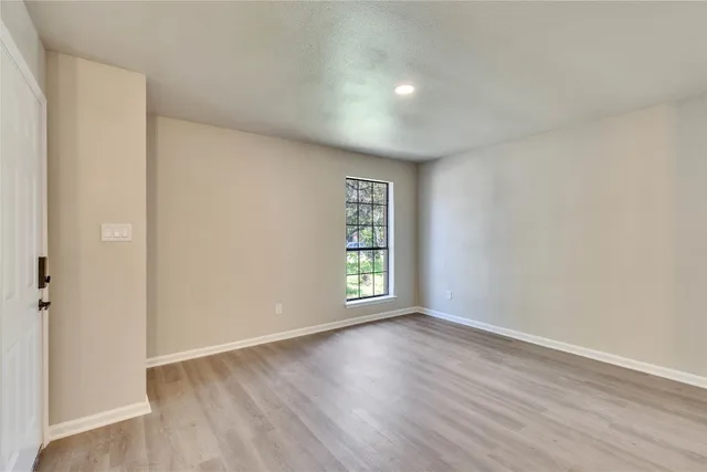 a view of an empty room with wooden floor and window