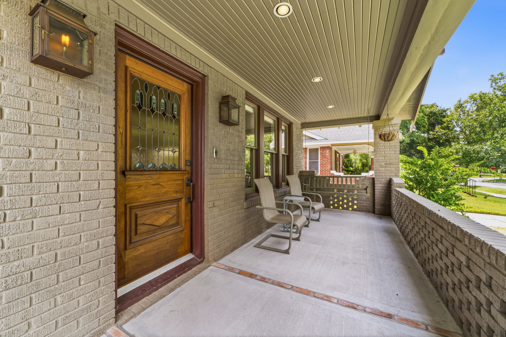 1521 Kipling Street Houston, TX 77006 - Photo 6 of 35 Charming front porch with a classic wooden door featuring stained glass. The space is framed by brick walls and offers cozy seating. Ideal for relaxing outdoors.