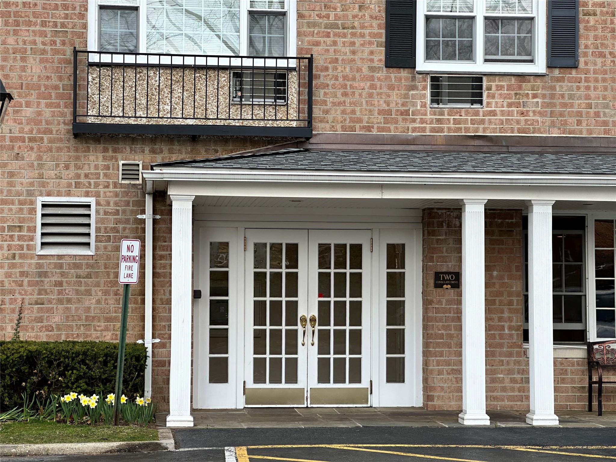 Entrance to property featuring a balcony, brick siding, a shingled roof, and french doors
