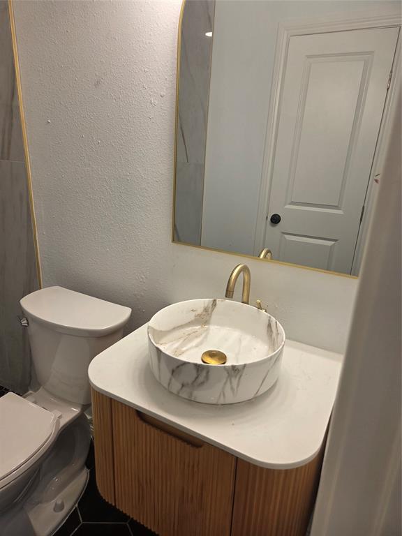 2108 Blake Avenue Dallas, TX 75228 - Photo 7 of 13 Primary bathroom vanity featuring a vessel sink with a gold-tone faucet, a wood-finish base cabinet, and a white countertop
