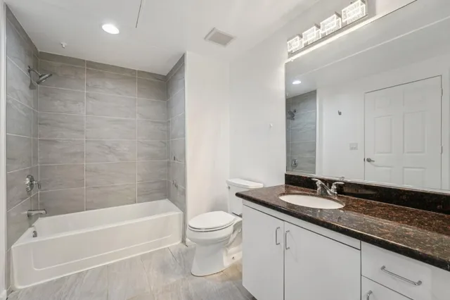 a bathroom with a granite countertop sink a toilet a mirror a bathtub and shower
