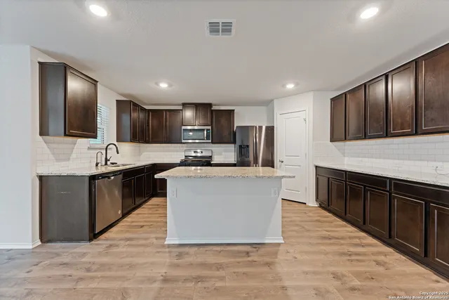 a large kitchen with stainless steel appliances granite countertop a stove a sink dishwasher a microwave oven and a refrigerator with wooden cabinets