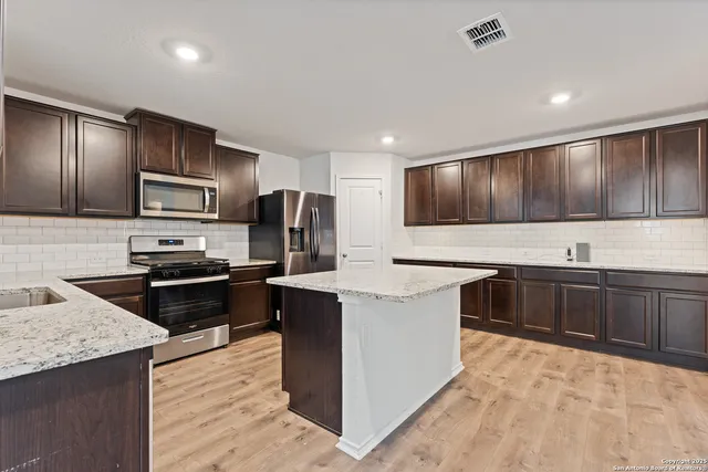 a kitchen with stainless steel appliances granite countertop a stove top oven a sink dishwasher a refrigerator and a oven with wooden cabinets