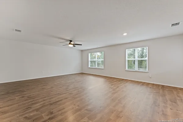 an empty room with wooden floor ceiling fan and windows