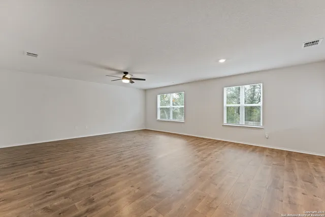 an empty room with wooden floor ceiling fan and windows