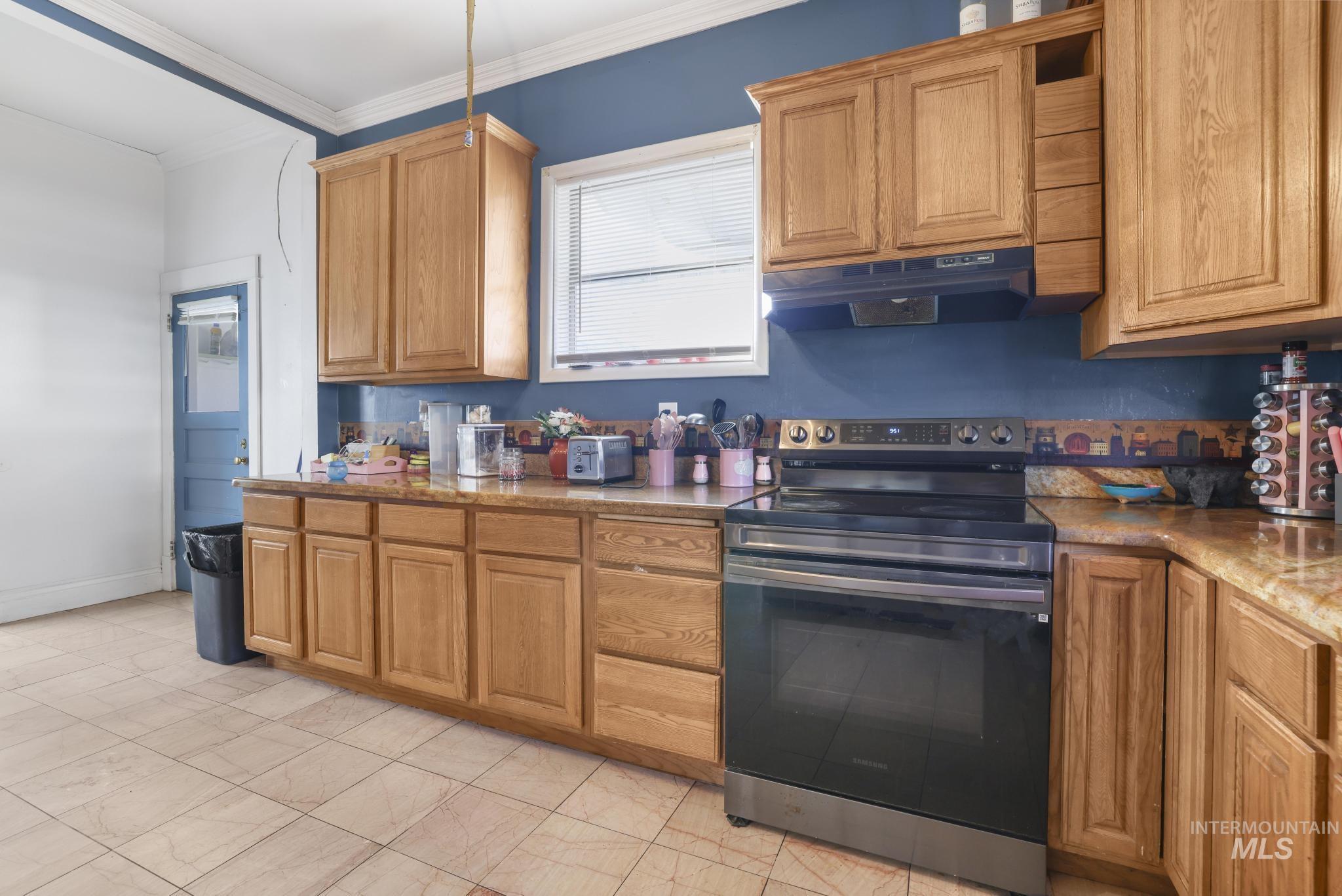 242 8th Avenue East Twin Falls, ID 83301 - Photo 13 of 35 Kitchen with electric range, ornamental molding, under cabinet range hood, brown cabinetry, and light stone countertops