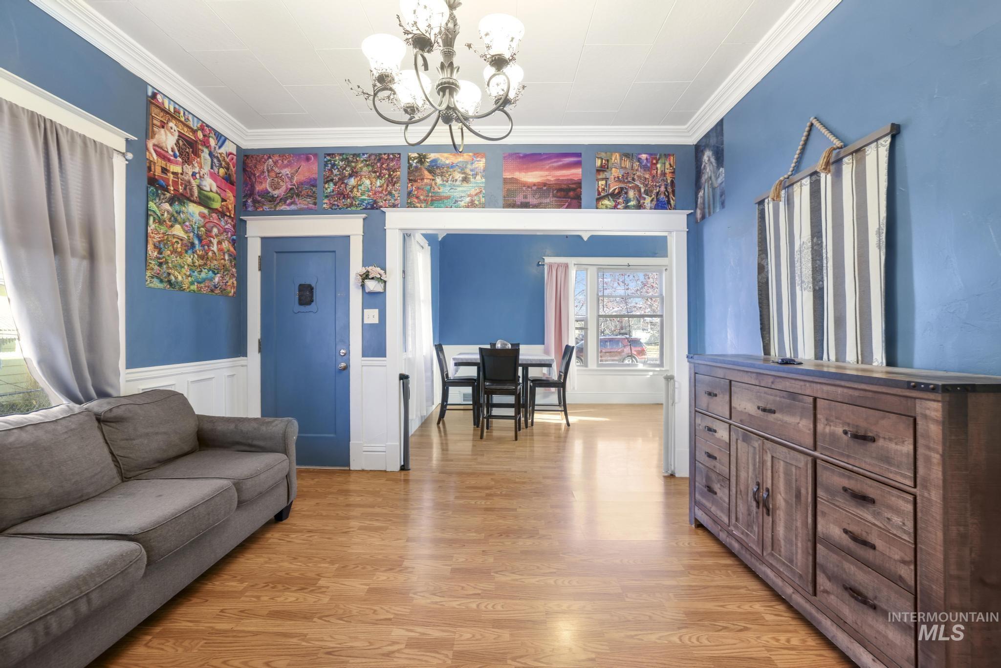 242 8th Avenue East Twin Falls, ID 83301 - Photo 4 of 35 Living room featuring a wainscoted wall, a chandelier, light wood finished floors, ornamental molding, and a decorative wall