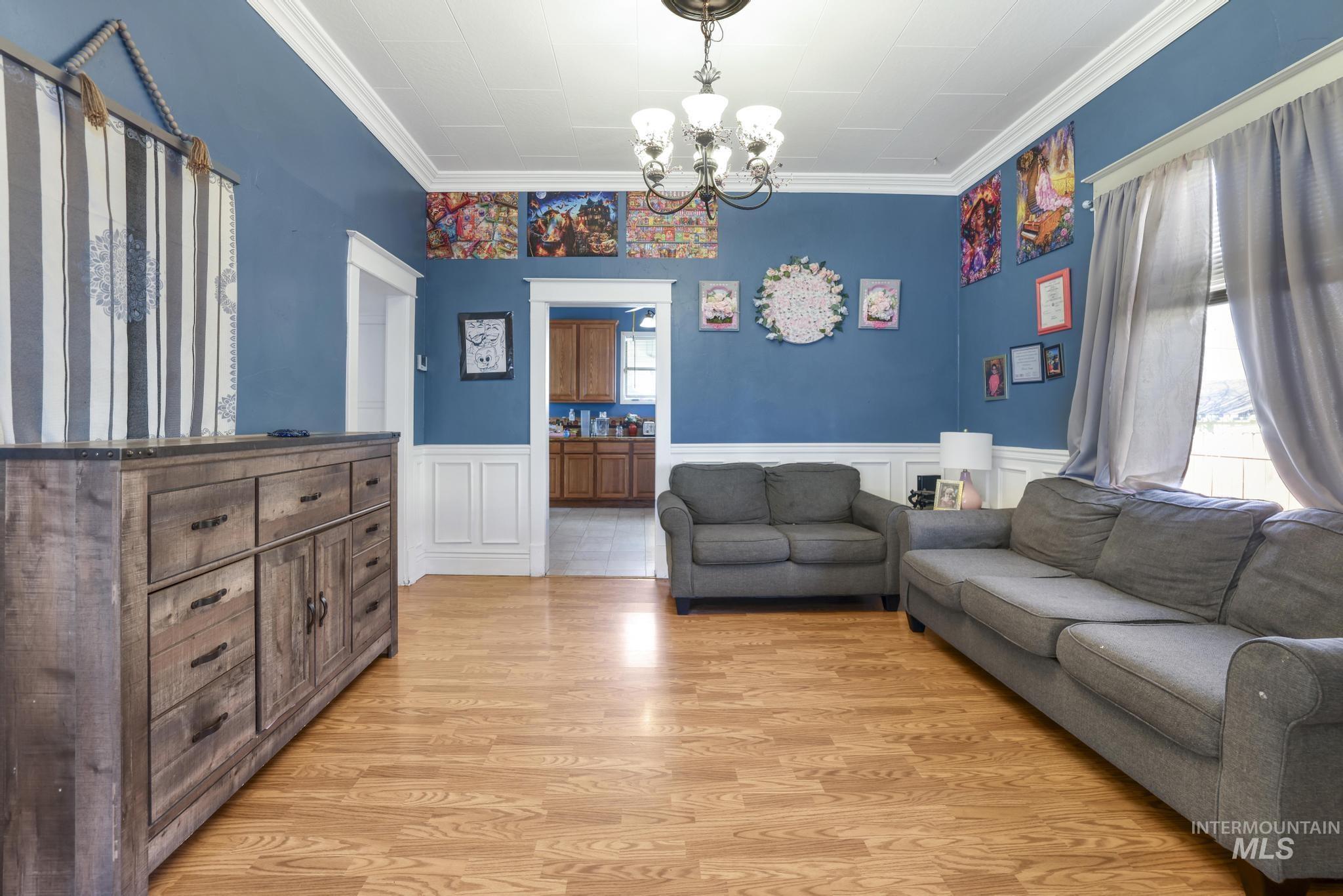 242 8th Avenue East Twin Falls, ID 83301 - Photo 5 of 35 Living room with a chandelier, light wood finished floors, a wainscoted wall, and ornamental molding