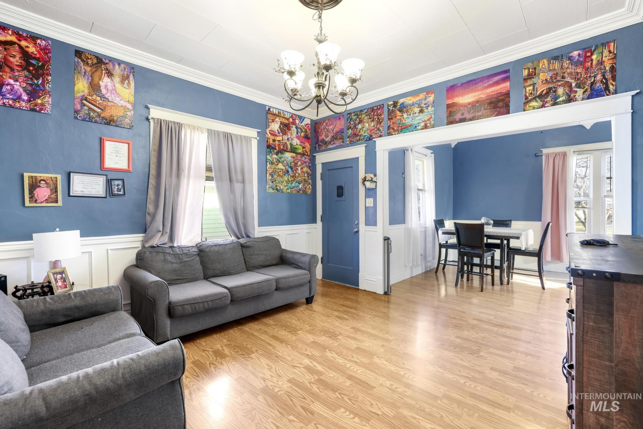 242 8th Avenue East Twin Falls, ID 83301 - Photo 6 of 35 Living room featuring light wood-type flooring, a chandelier, wainscoting, crown molding, and a decorative wall