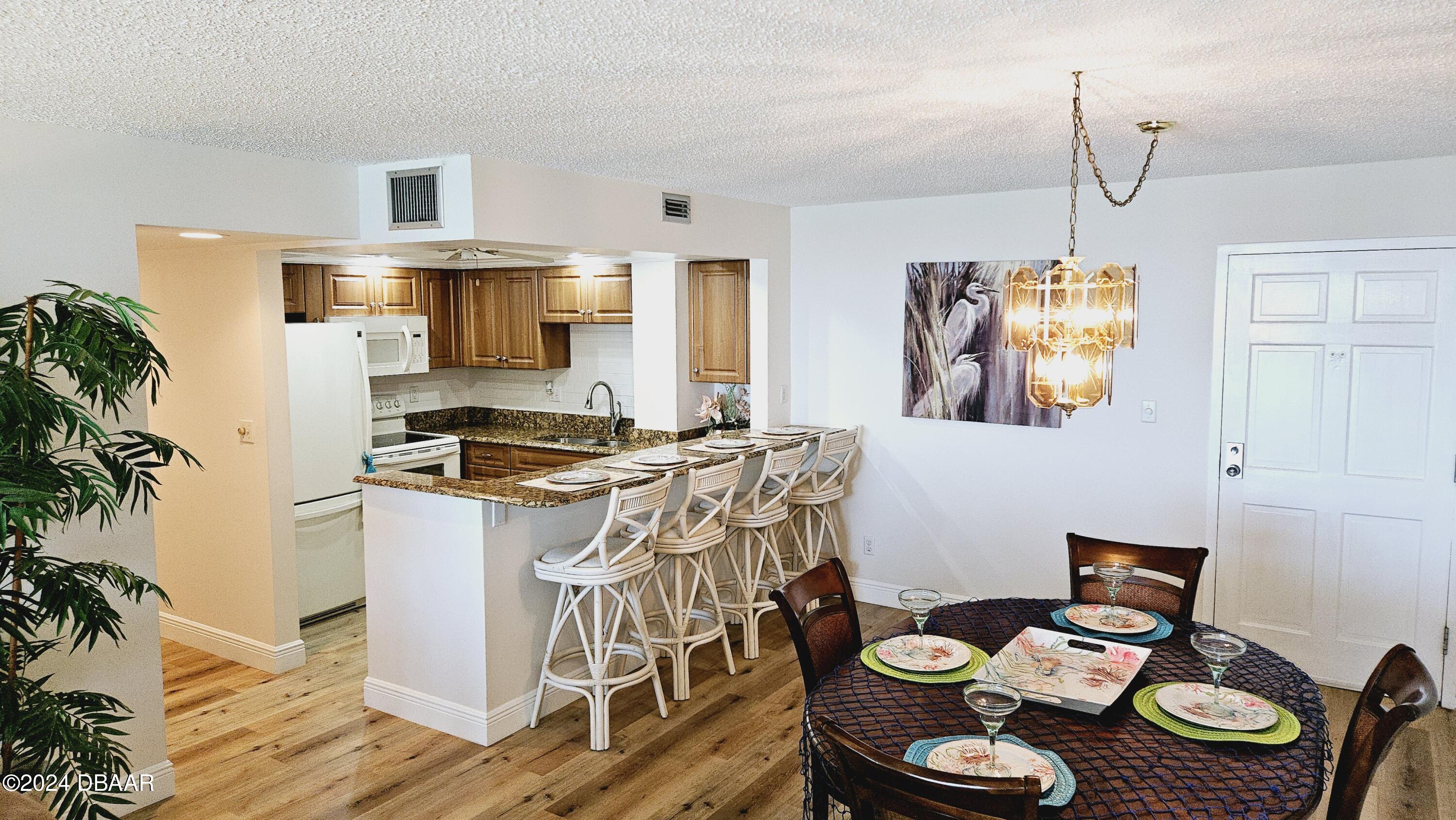 1575 Ocean Shore Boulevard, Unit 1003 Ormond Beach, FL 32176 - Photo 9 of 40 a kitchen with granite countertop a white stove top oven a dining table and chairs with wooden floor