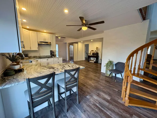 a living room with chairs kitchen view and a wooden floor