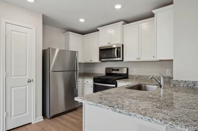 a kitchen with stainless steel appliances granite countertop a refrigerator a stove a sink and a white cabinets