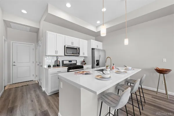 a white kitchen with stainless steel appliances kitchen island granite countertop a stove a sink a dining table and chairs with wooden floor
