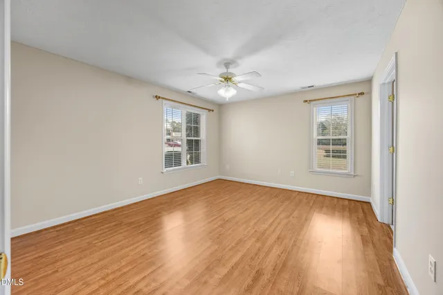 an empty room with wooden floor fireplace and windows