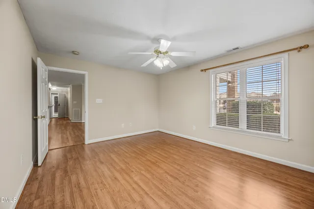 a view of an empty room with wooden floor and a ceiling fan