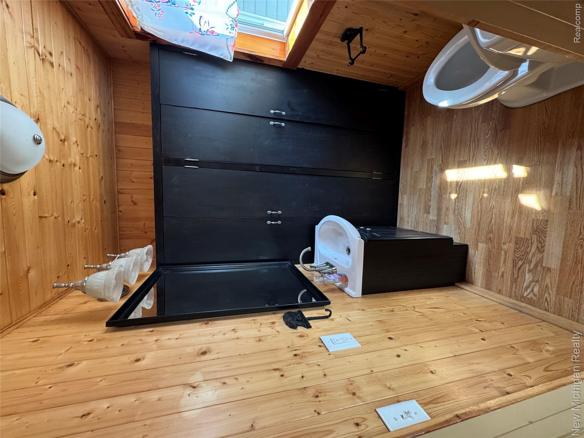 7415 Farrand Road Clio, MI 48420 - Photo 36 of 46 Wood-finish flooring, wood paneling, black vanity with integrated sink, black wall-mounted mirror, and overhead lighting