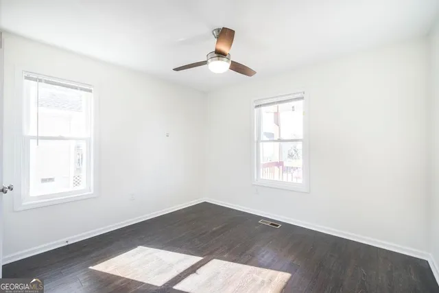 an empty room with wooden floor ceiling fan and window