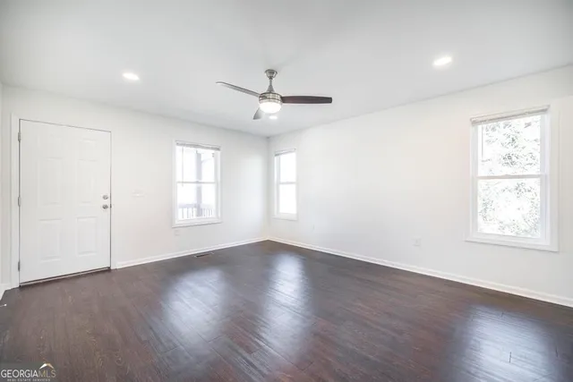 an empty room with wooden floor ceiling fan and windows