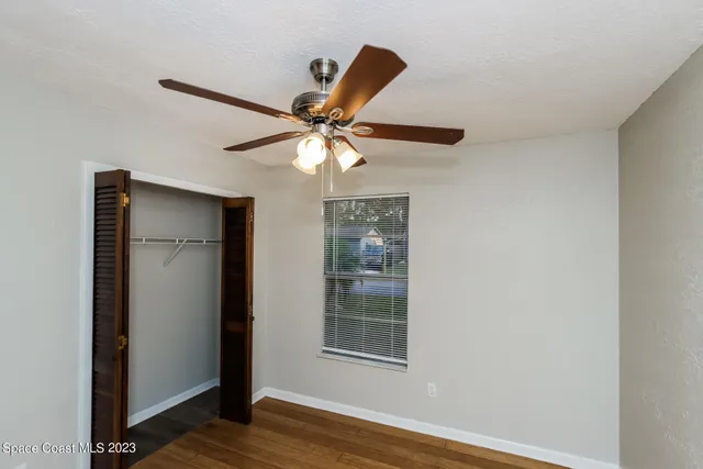 an empty room with wooden floor fan and windows
