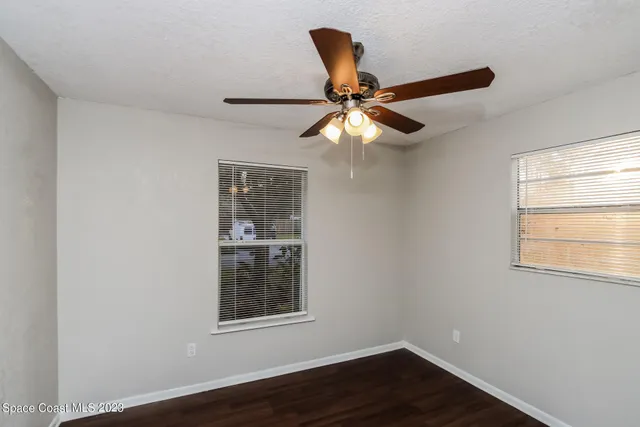 an empty room with wooden floor fan and windows