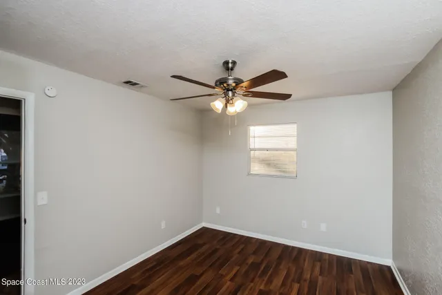 an empty room with wooden floor fan and windows