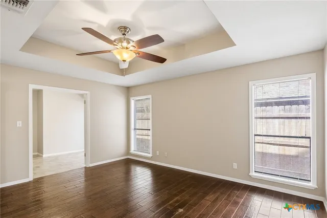 an empty room with wooden floor chandelier fan and windows