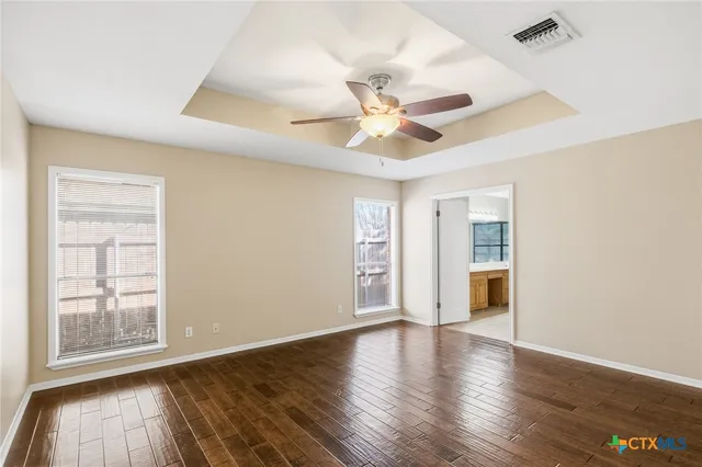 an empty room with wooden floor chandelier fan and windows