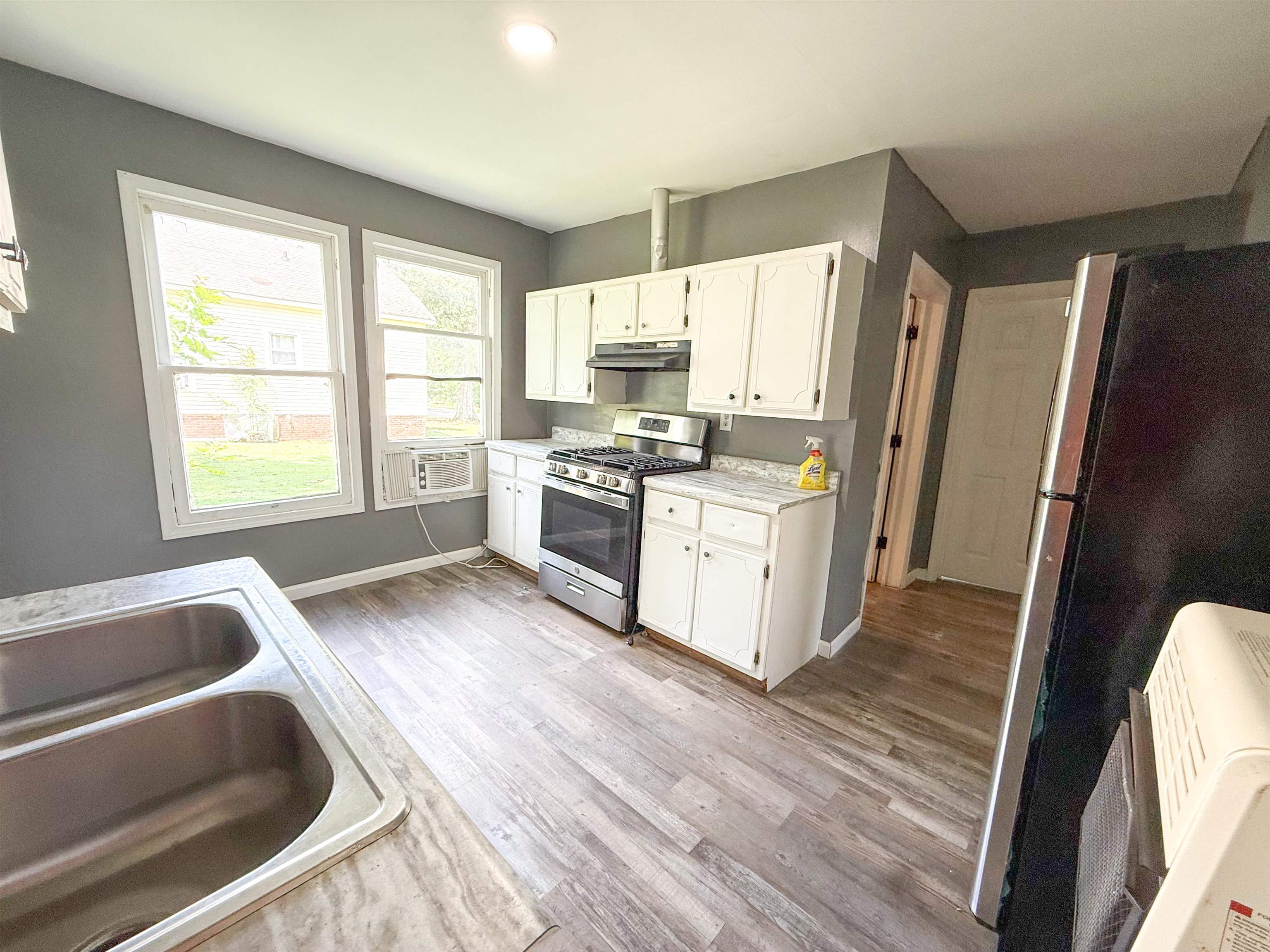 403 Sharp Street Corinth, MS 38834 - Photo 2 of 9 Kitchen featuring white cabinetry, wood-finish flooring, a double basin stainless steel sink, and a gas range with a matching range hood