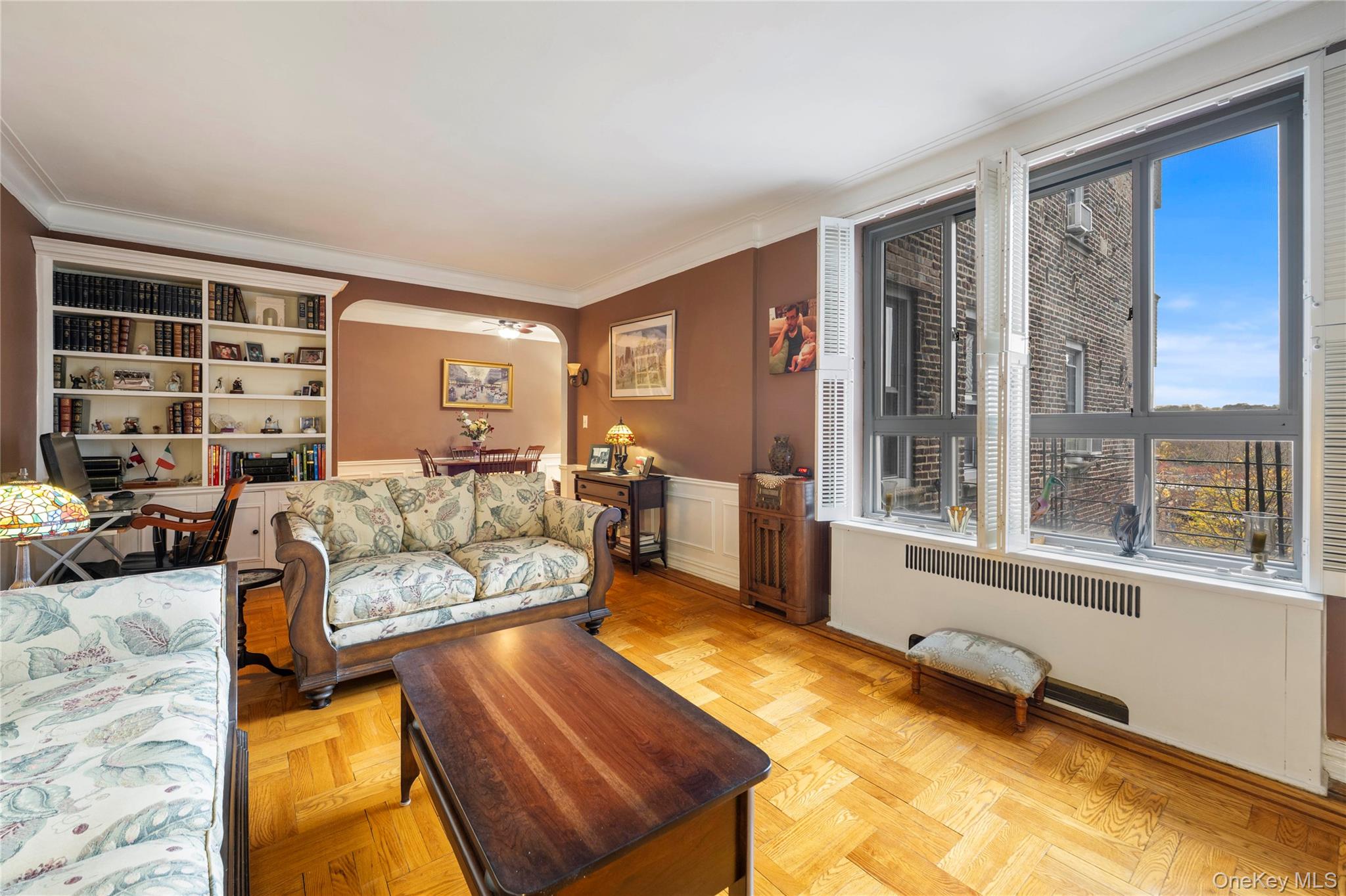 Living area featuring arched walkways, radiator, crown molding, and a wainscoted wall