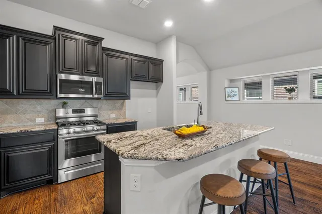 a kitchen with stainless steel appliances granite countertop a stove top oven a sink a refrigerator white cabinets and chairs