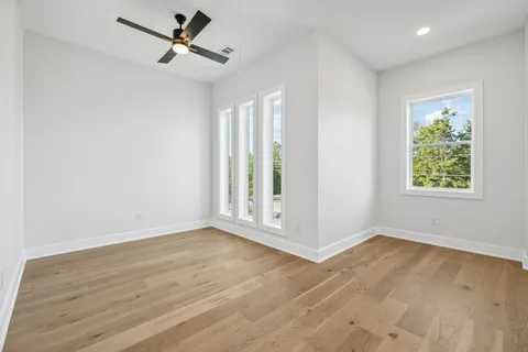 an empty room with wooden floor fan and windows